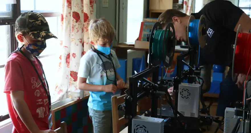 Campers watch a mentor at a 3D printer