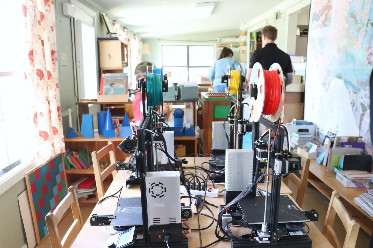 A row of 3D printers and their spools of filament down a classroom